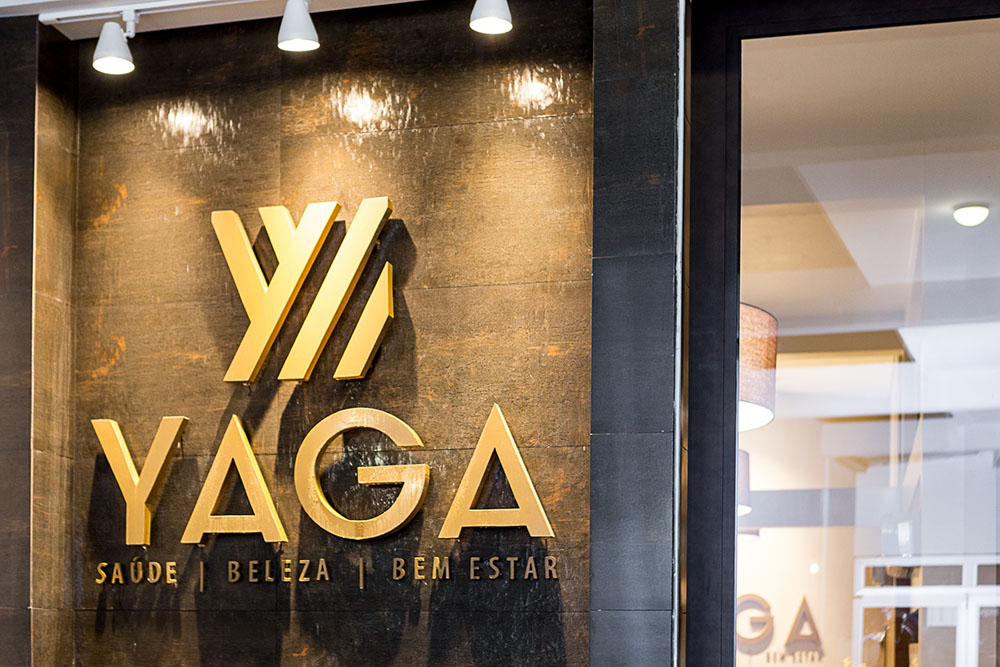 Recepção da Clínica Yaga com a marca em dourado sobre a parede de madeira